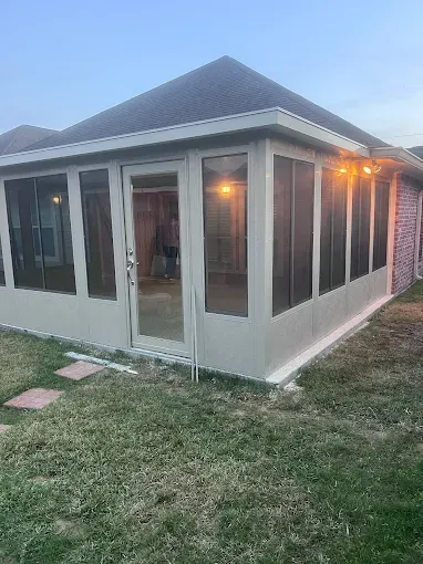 Screened-in porch with tan walls, glass door, and string lights, attached to a brick house, evening setting.
