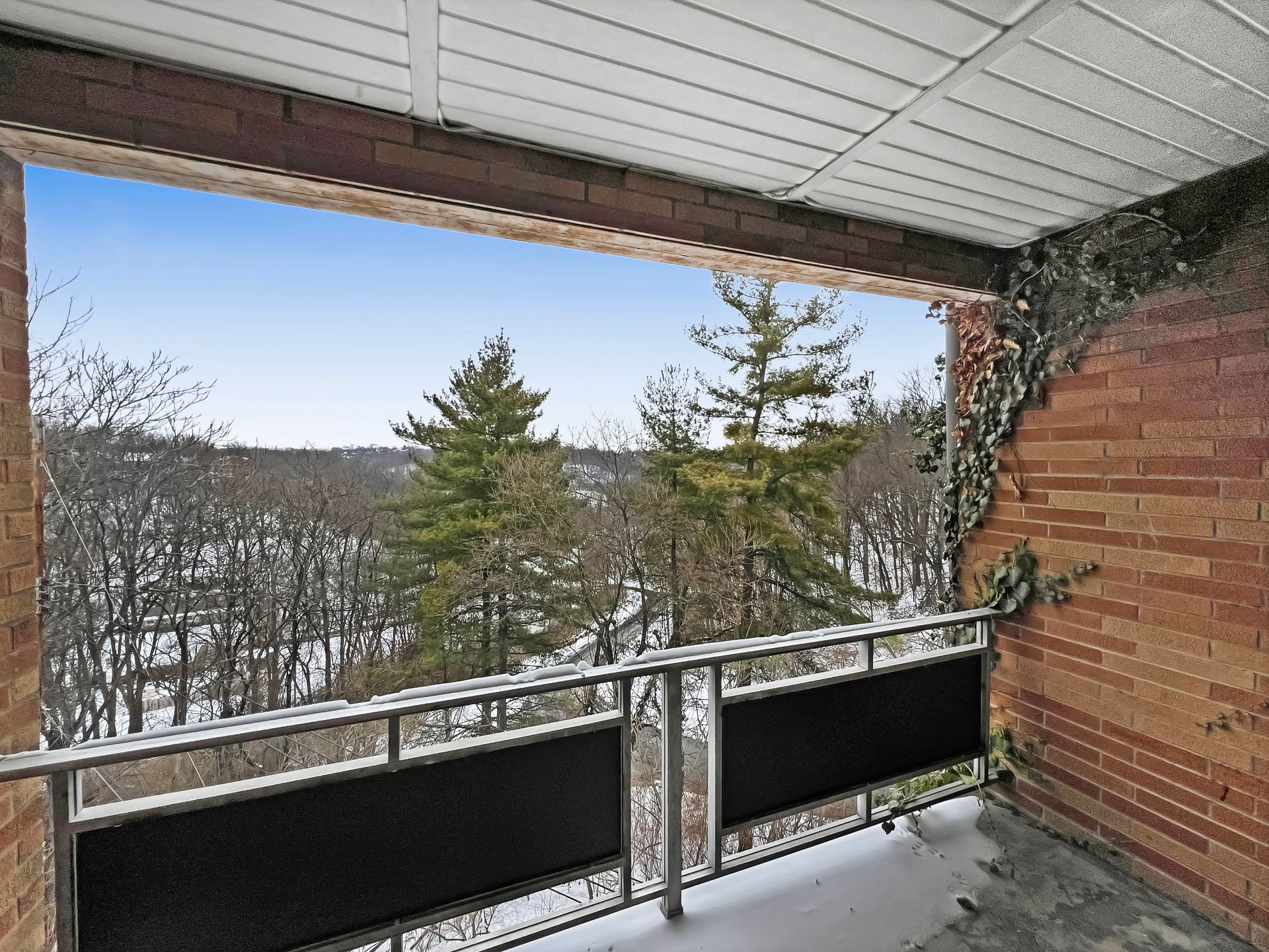 Balcony view of snowy trees and sky framed by brick walls and a metal railing.