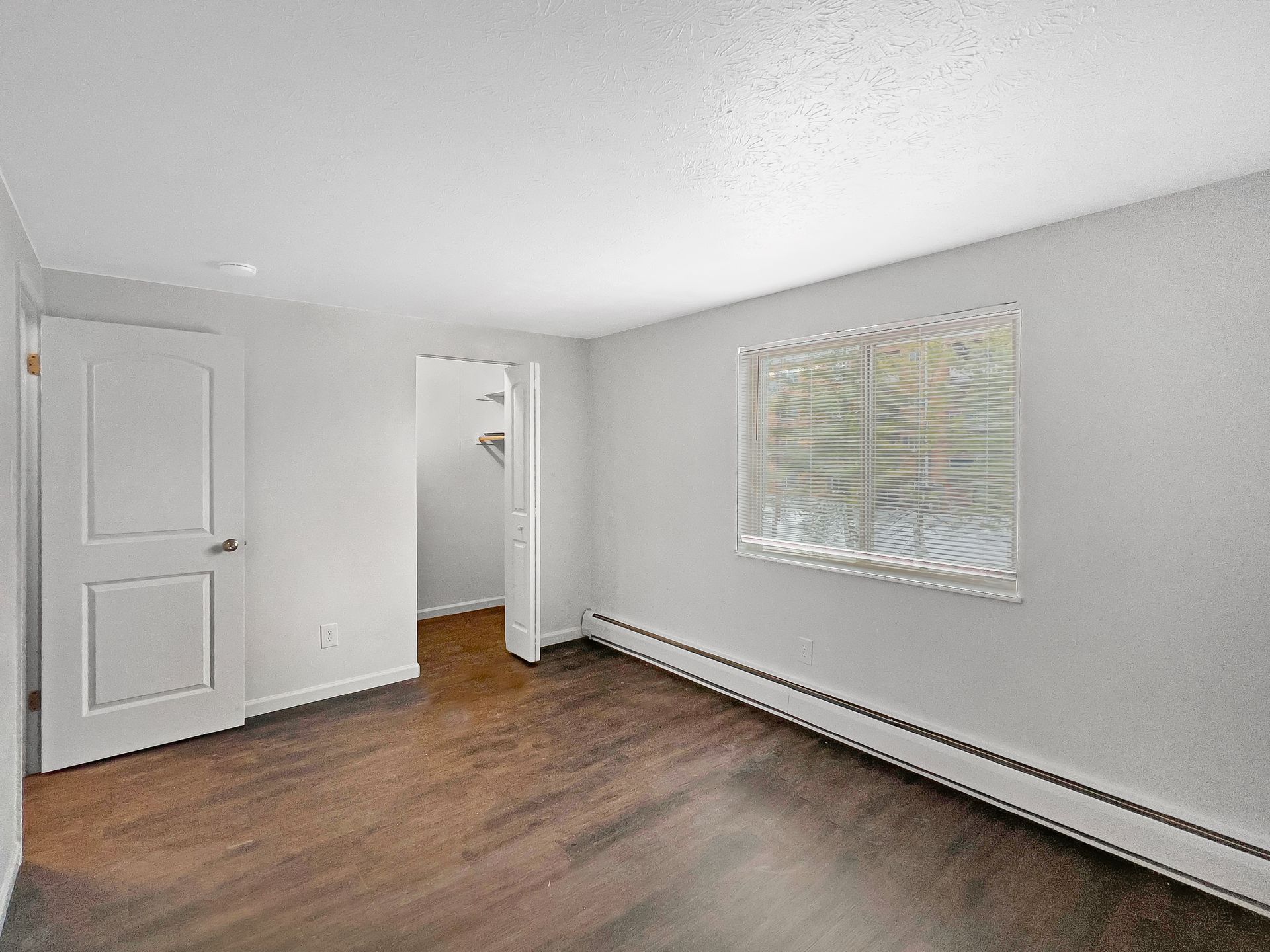 Empty, gray-walled room with a dark wood floor, a white door, and a glass block window.