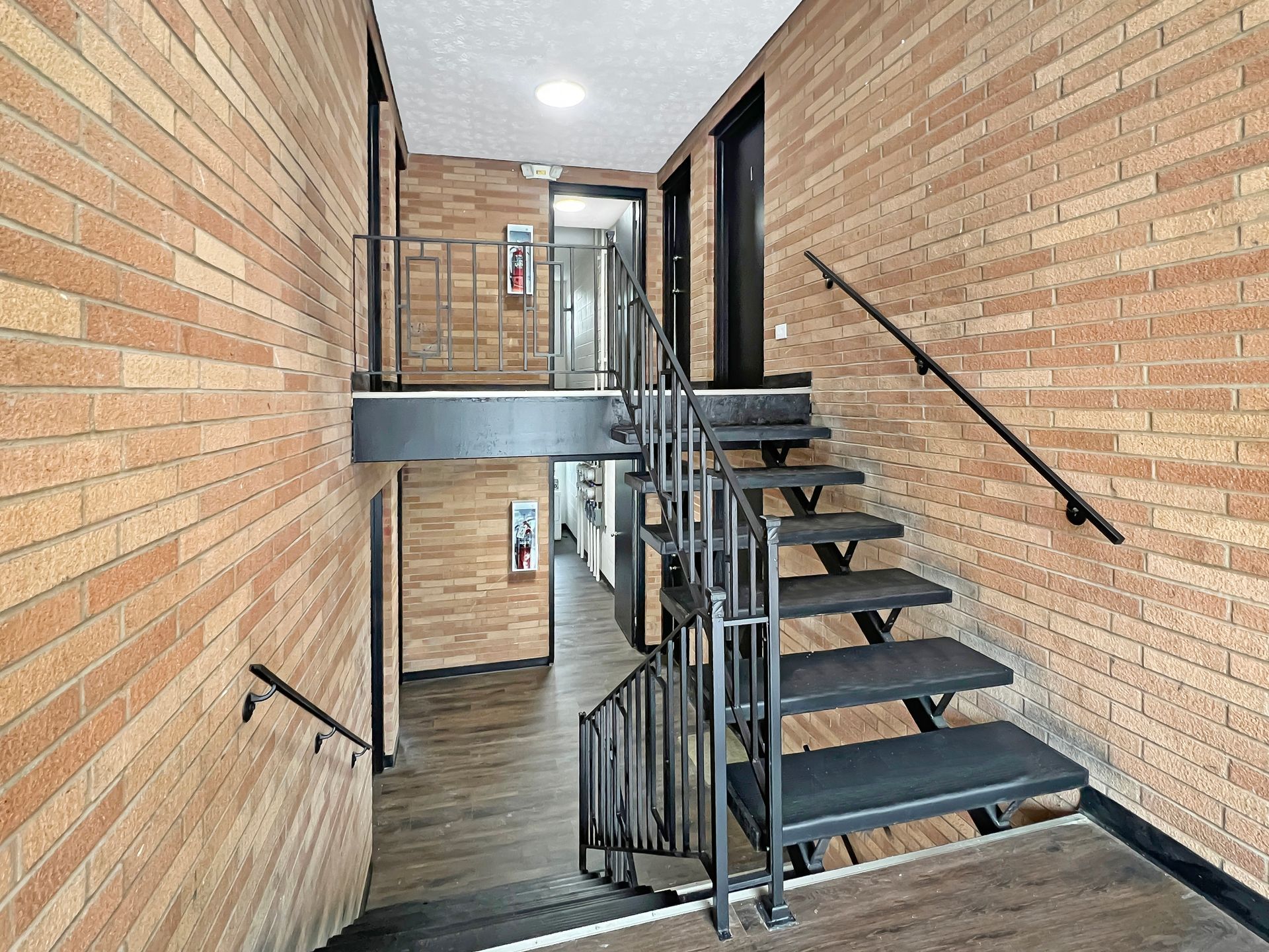 Stairwell with brick walls and black metal handrails and stairs. One landing leads to an open hallway.