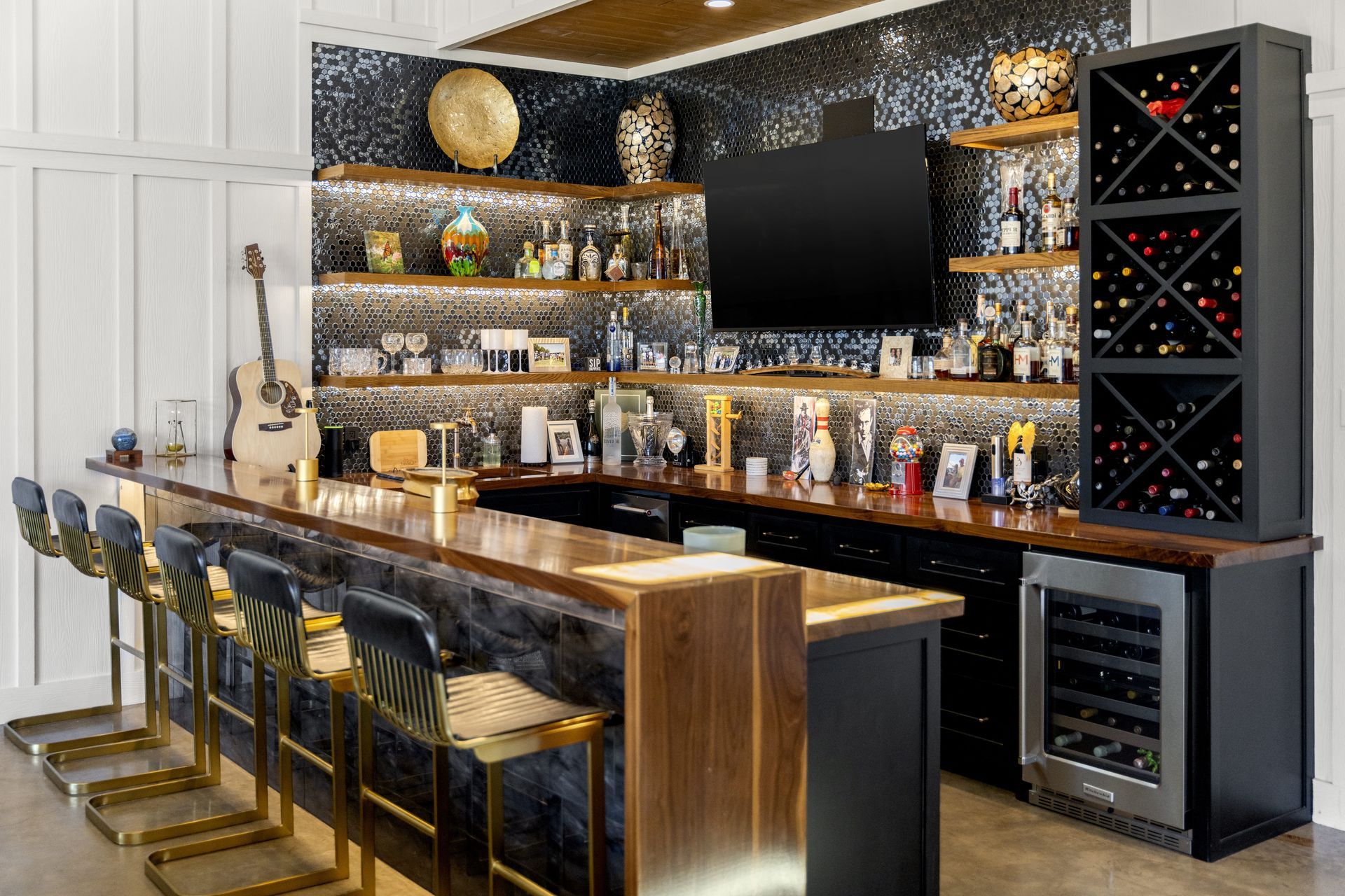 There is a bar with stools and a wine cooler in the middle of the room.