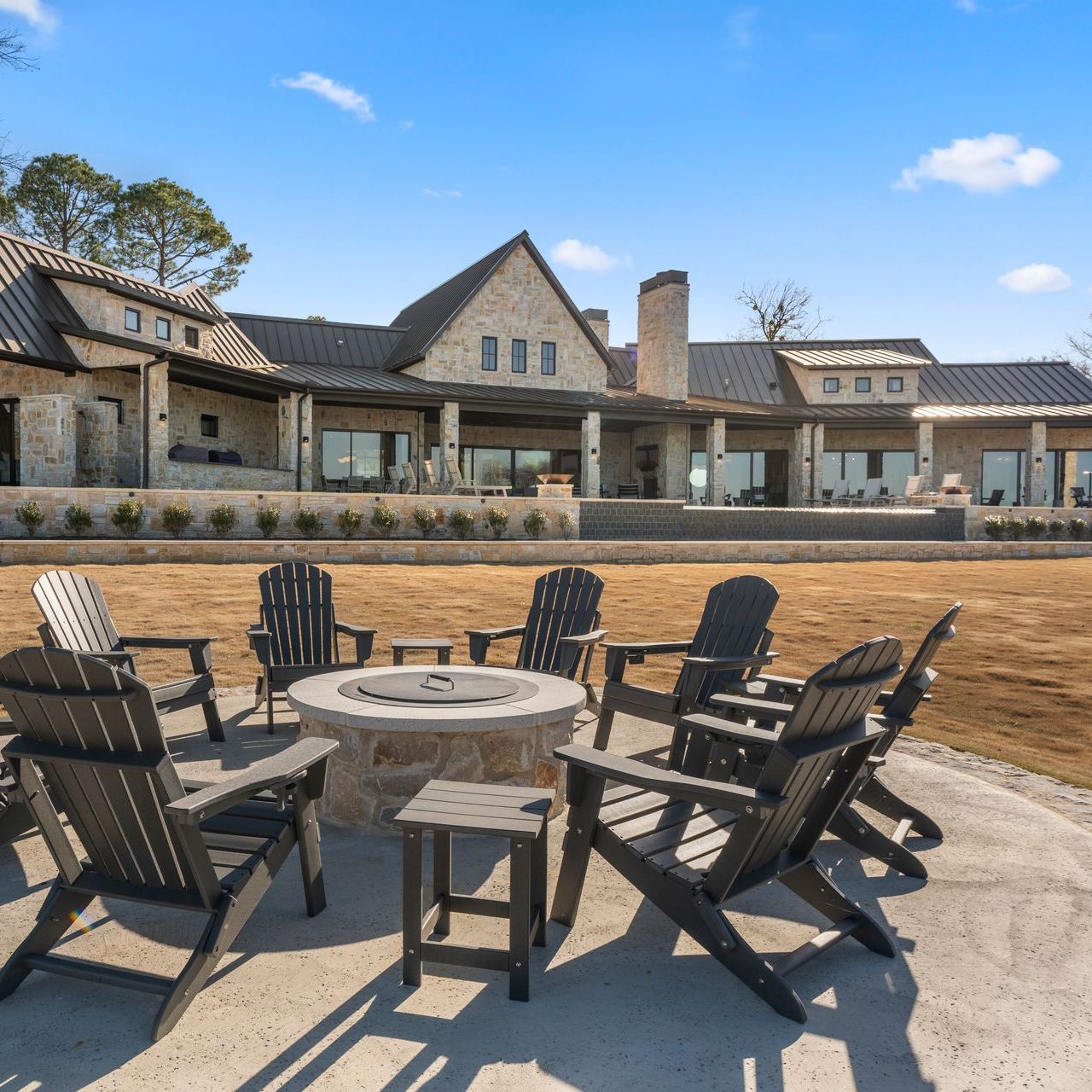 A group of chairs around a fire pit in front of a large house