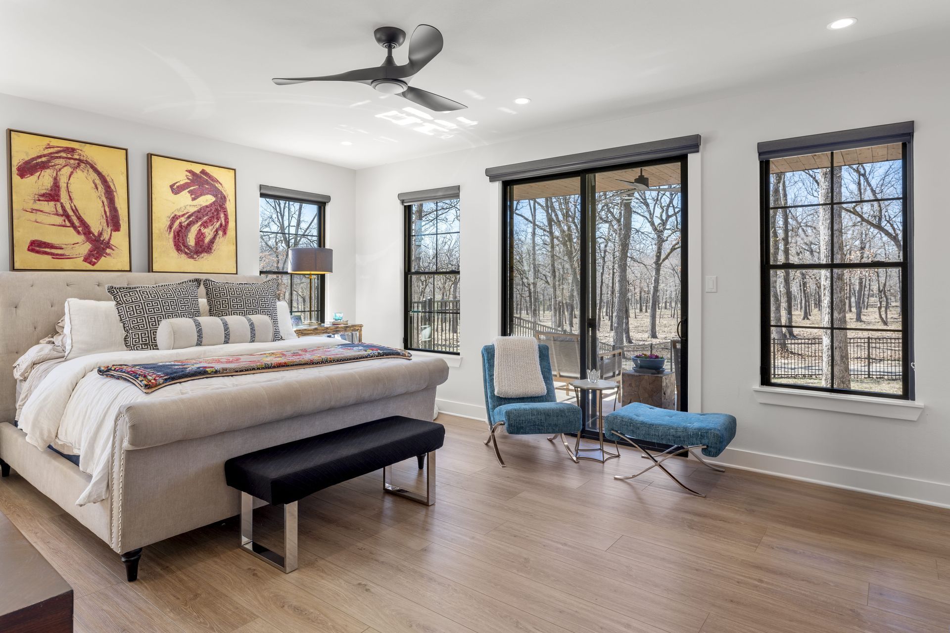 A bedroom with a king size bed , chairs , a bench and a ceiling fan.