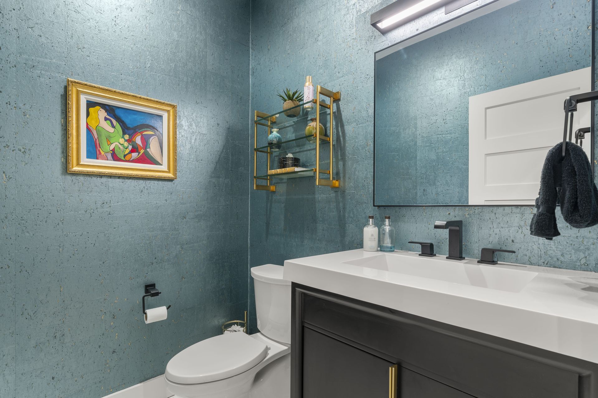 A bathroom with a toilet , sink , mirror and painting on the wall.