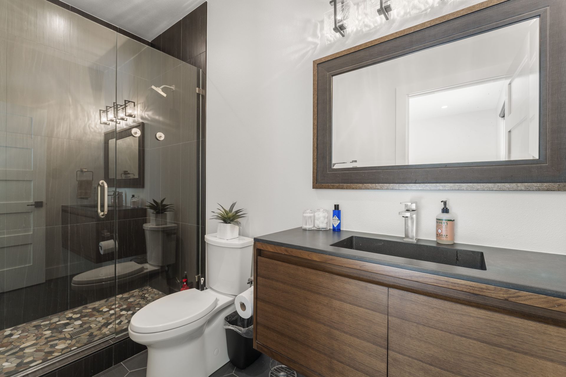 A bathroom with a toilet , sink , mirror and walk in shower.