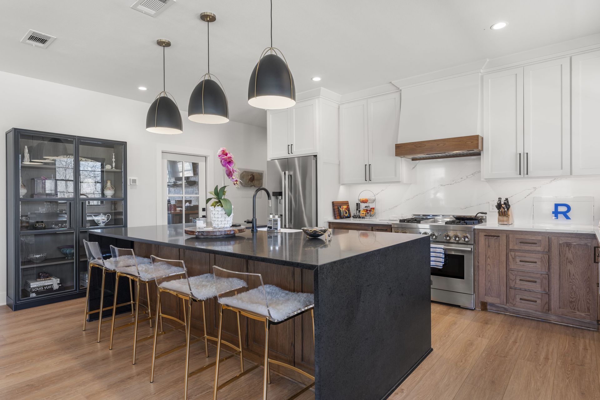 A kitchen with a large island , stools , a refrigerator and a stove.