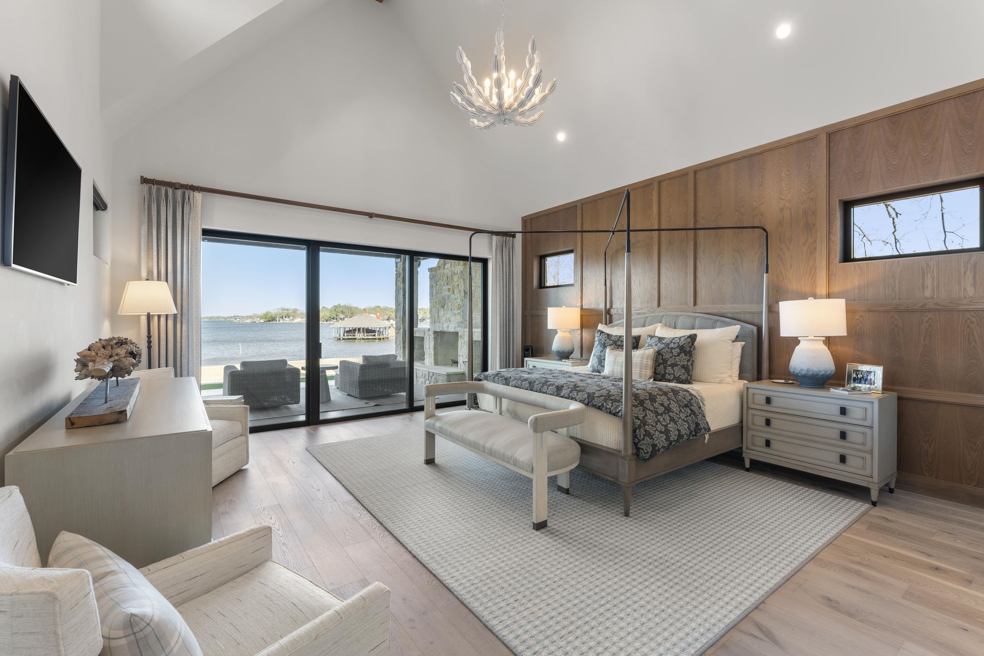 A large bedroom with a four poster bed , dresser , chair and television.