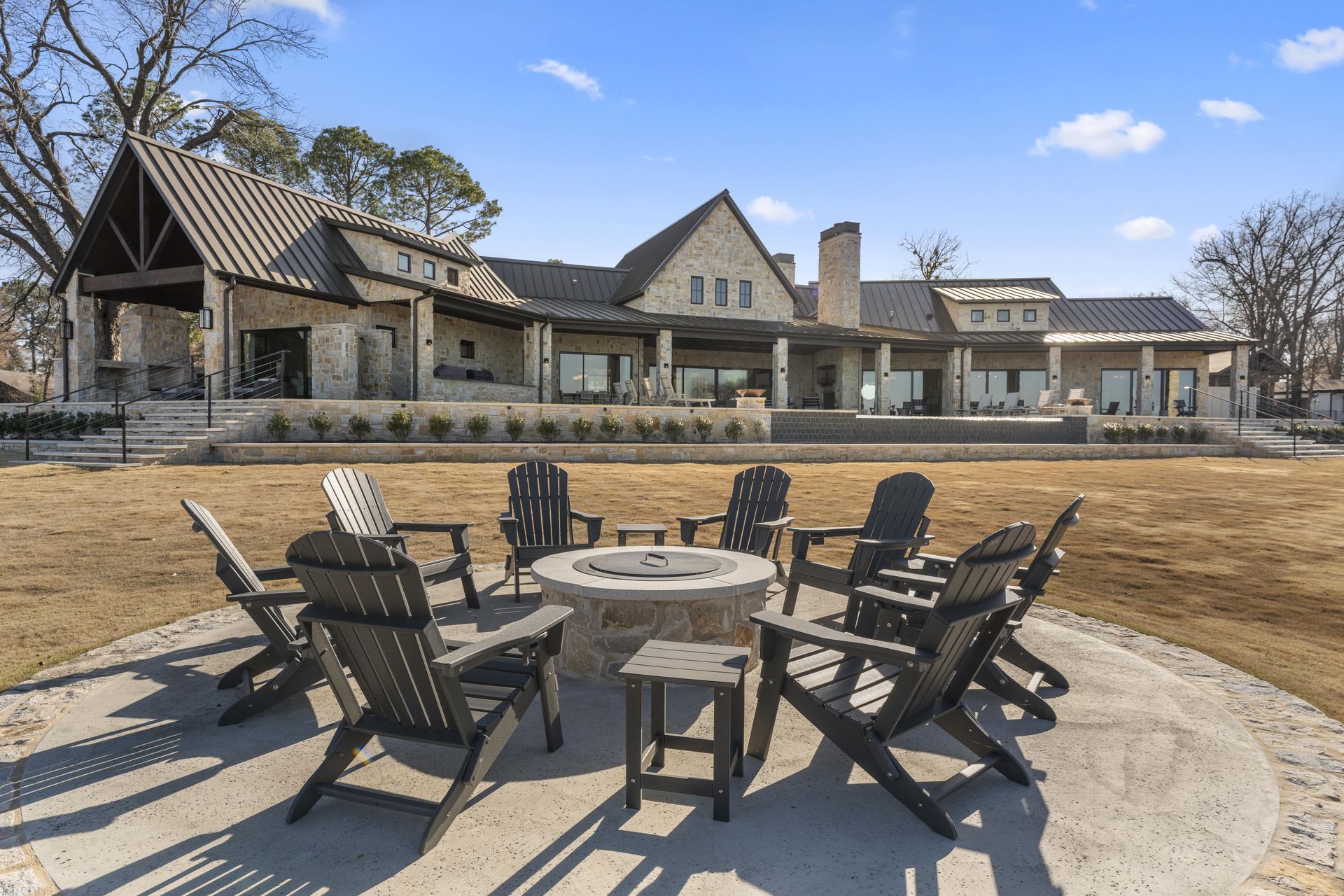 A group of chairs are sitting around a fire pit in front of a large house.