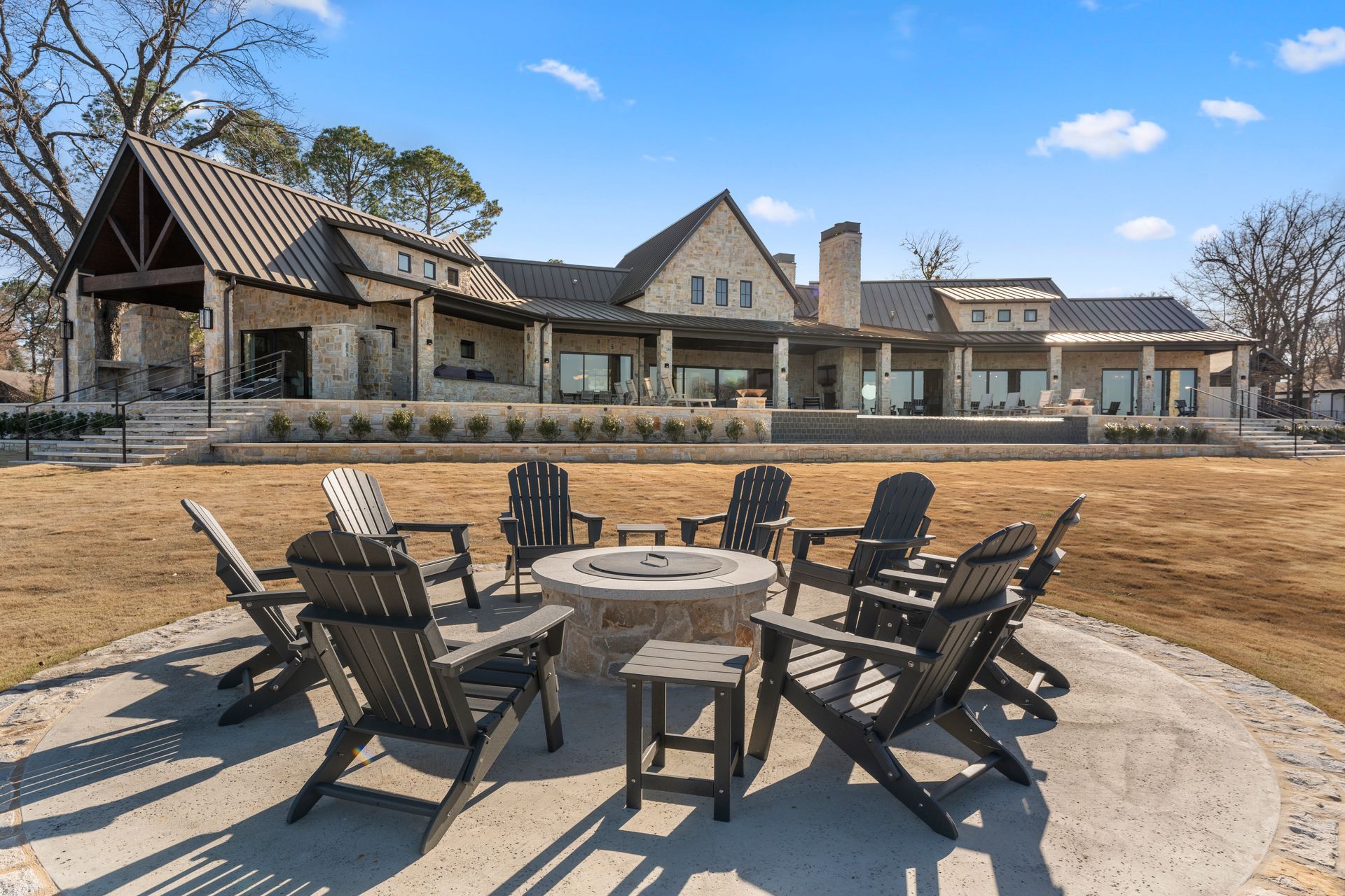 A group of chairs are sitting around a fire pit in front of a large house.