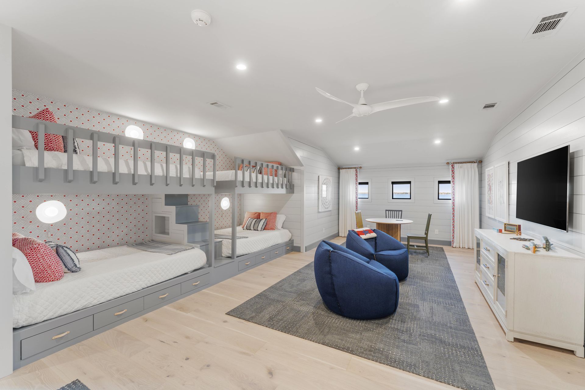 A room with bunk beds , chairs , a table and a television.