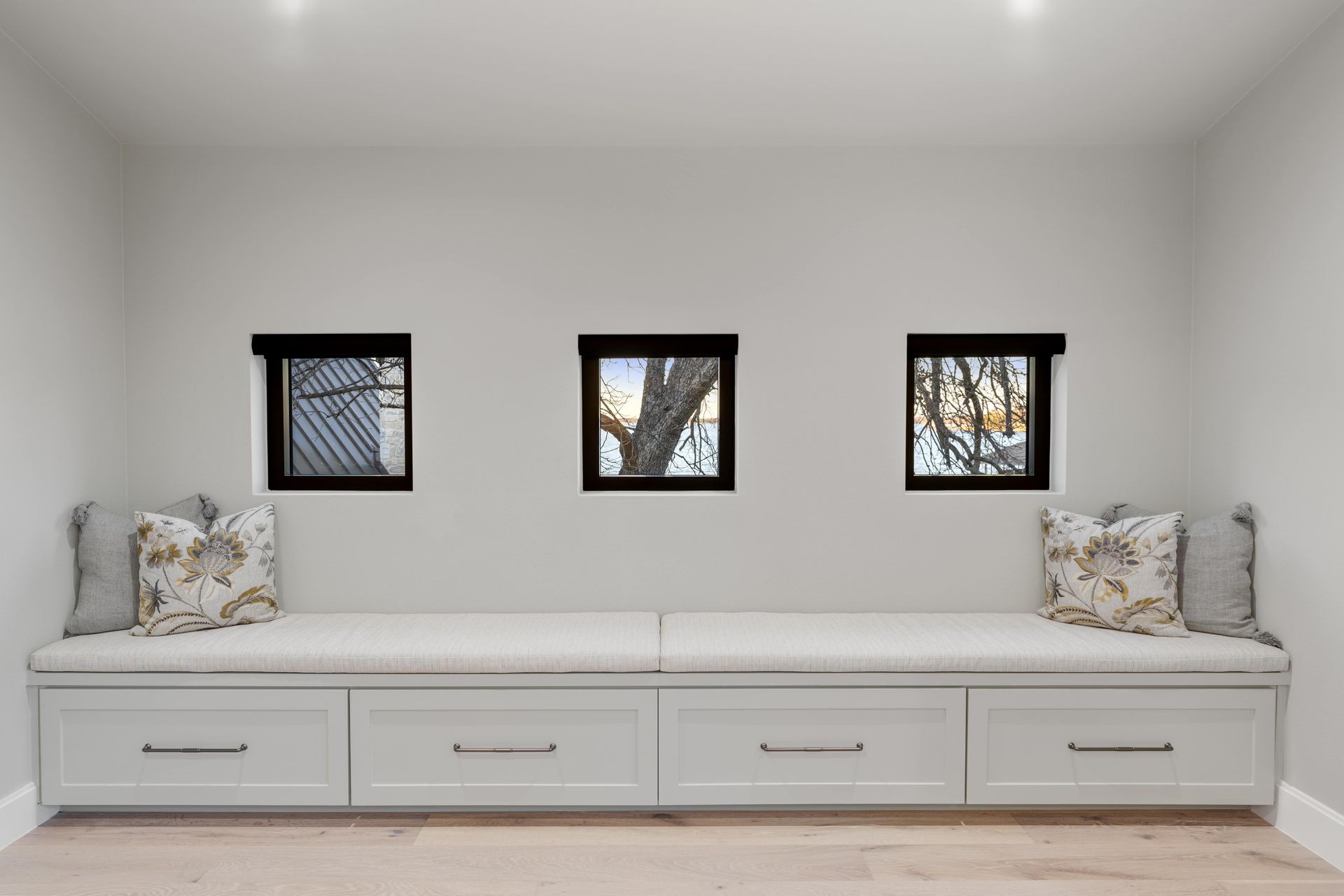 A room with a bench and three windows on the wall.