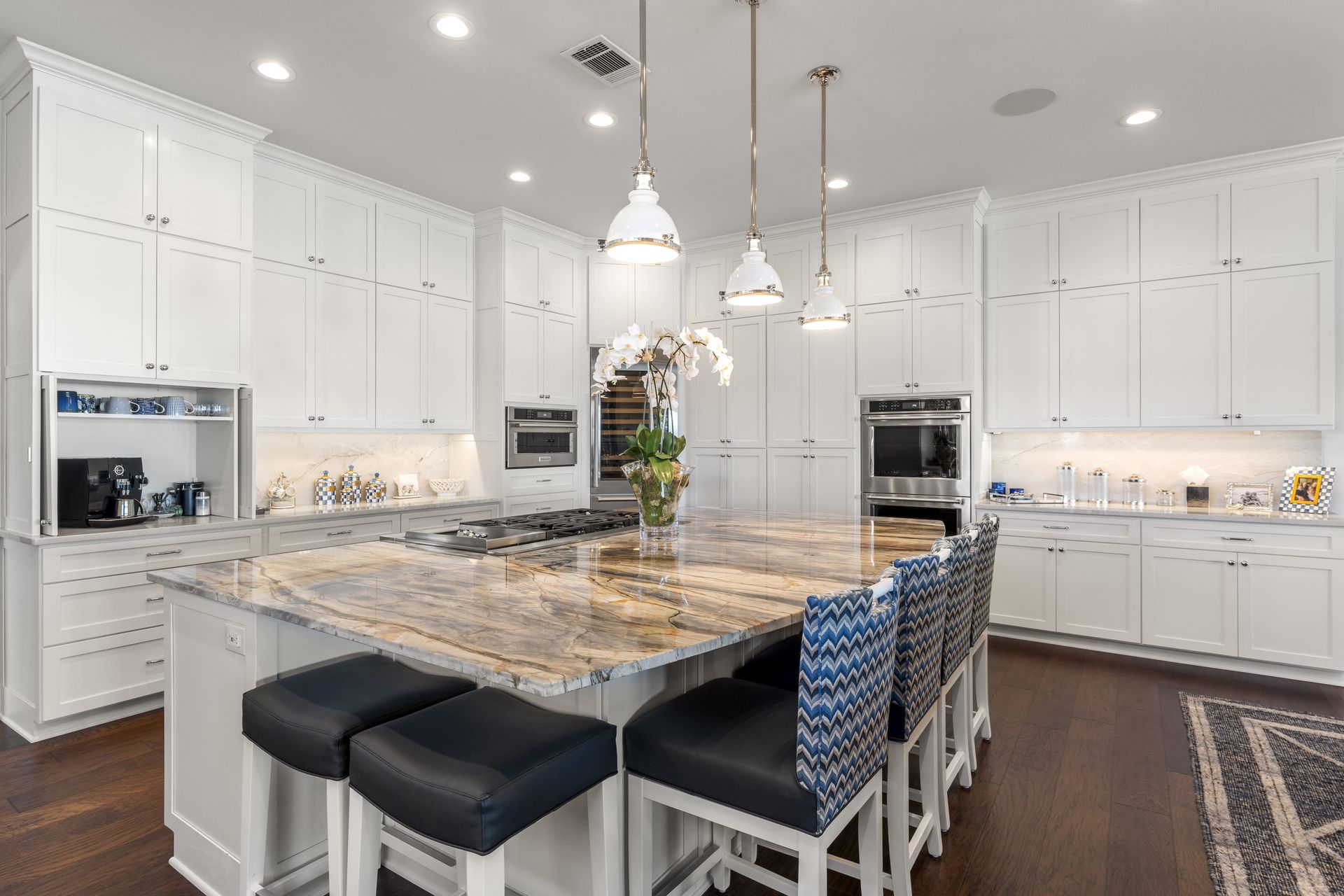 A kitchen with white cabinets , granite counter tops , and stools.