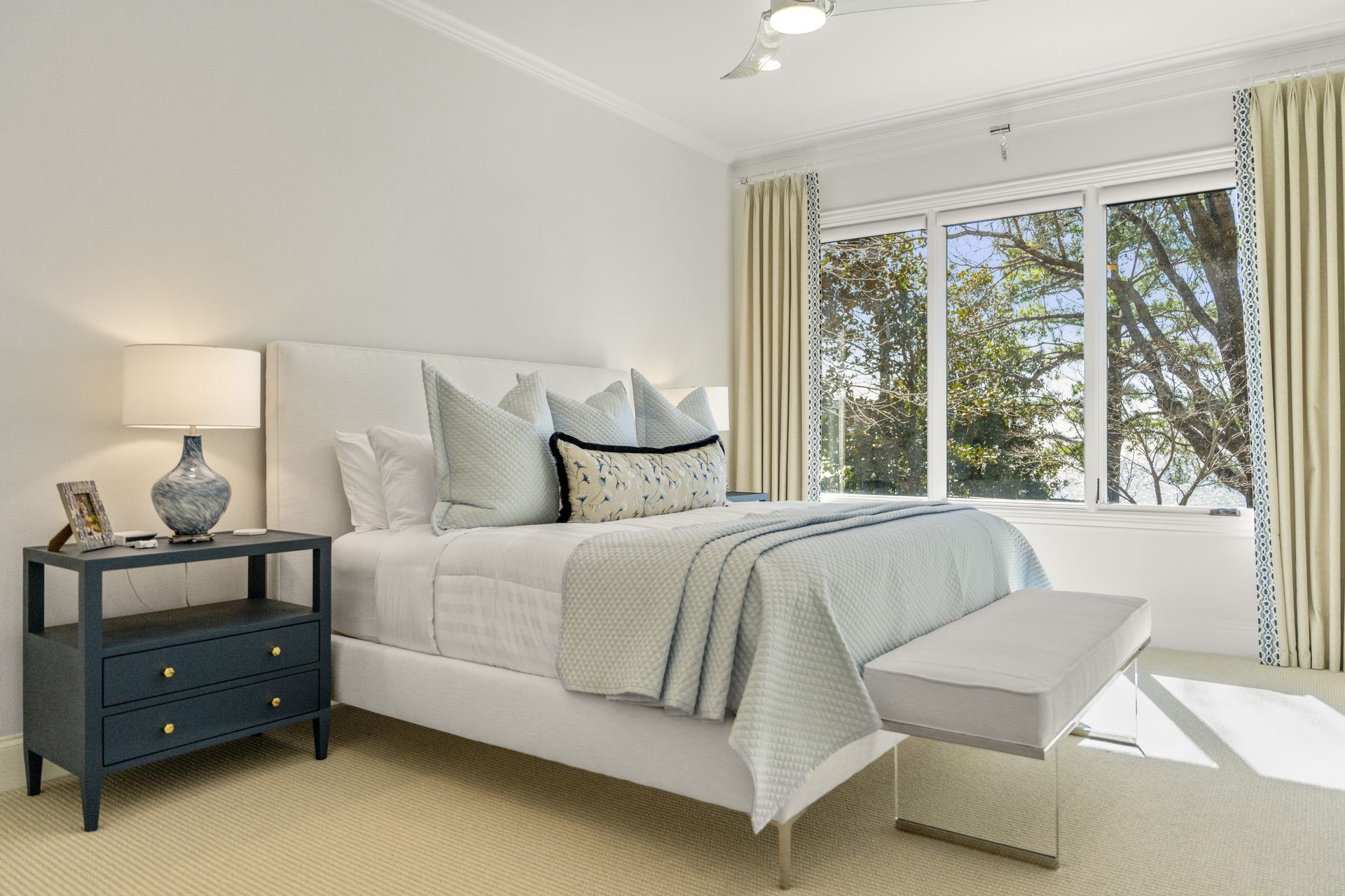 A bedroom with a bed , nightstand , lamp and window.