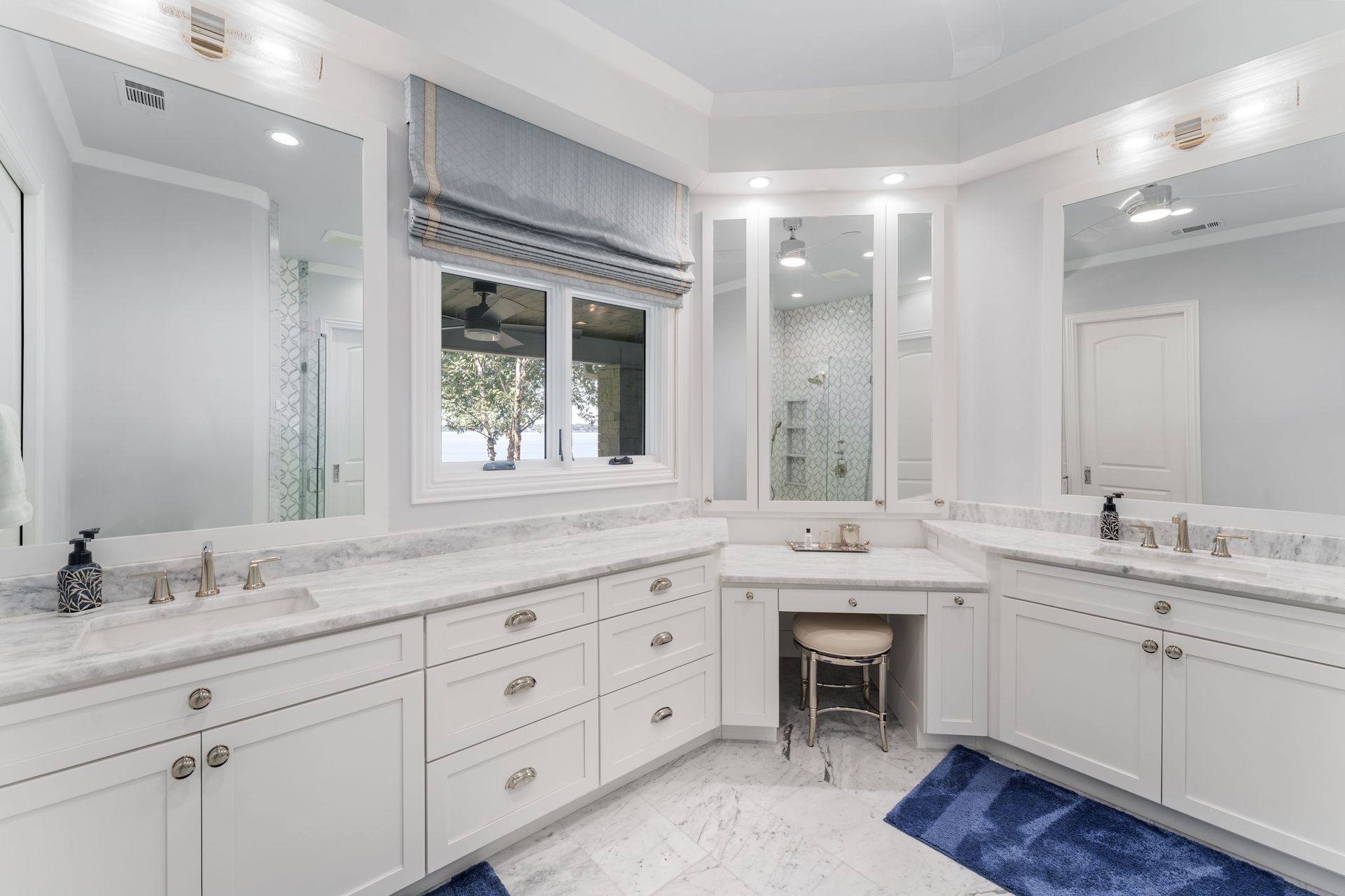 A bathroom with two sinks , two mirrors and a blue rug.