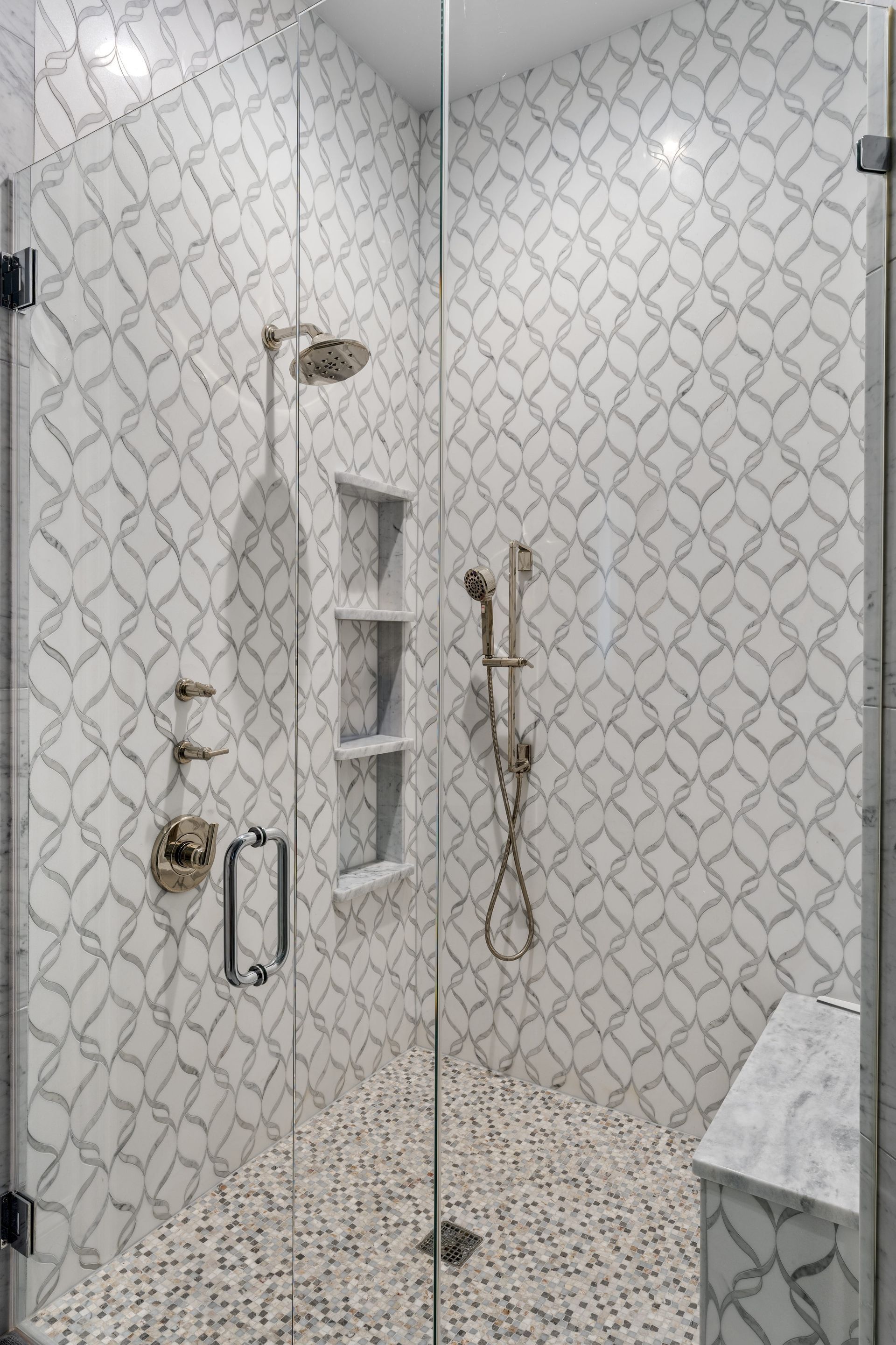 A walk in shower with a glass door and marble tiles.