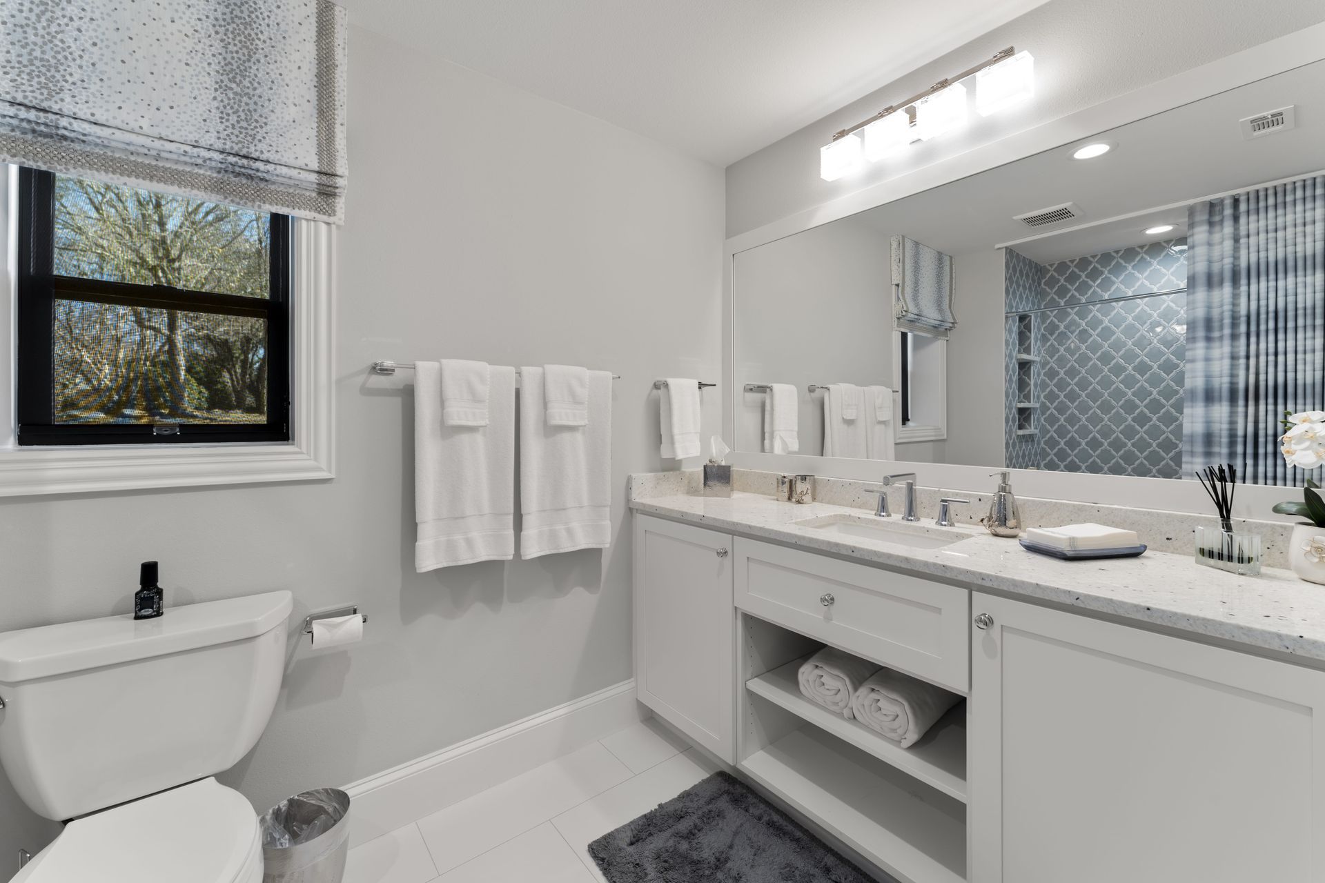 A bathroom with a toilet , sink , mirror and window.