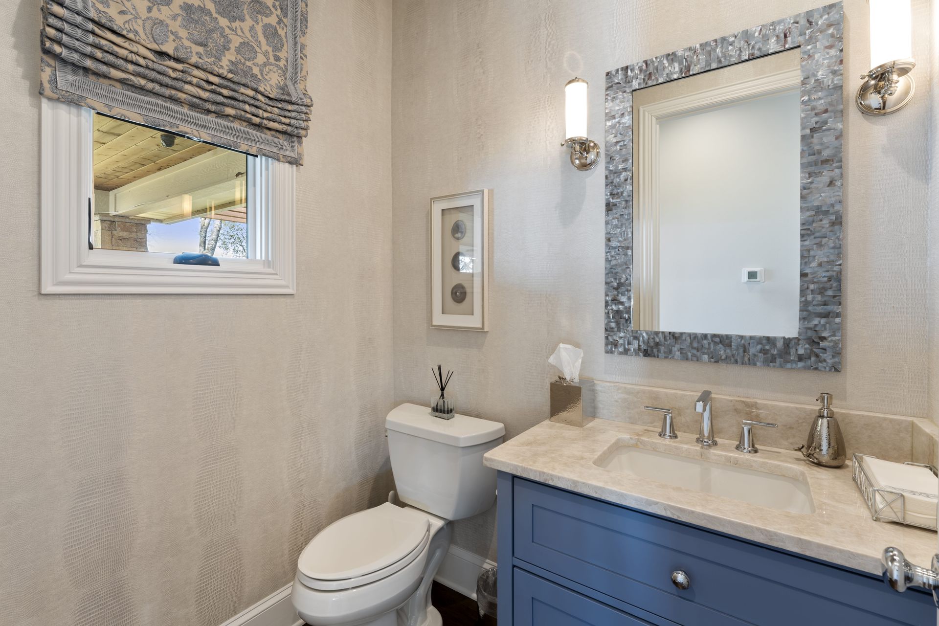 A bathroom with a toilet , sink , mirror and window.