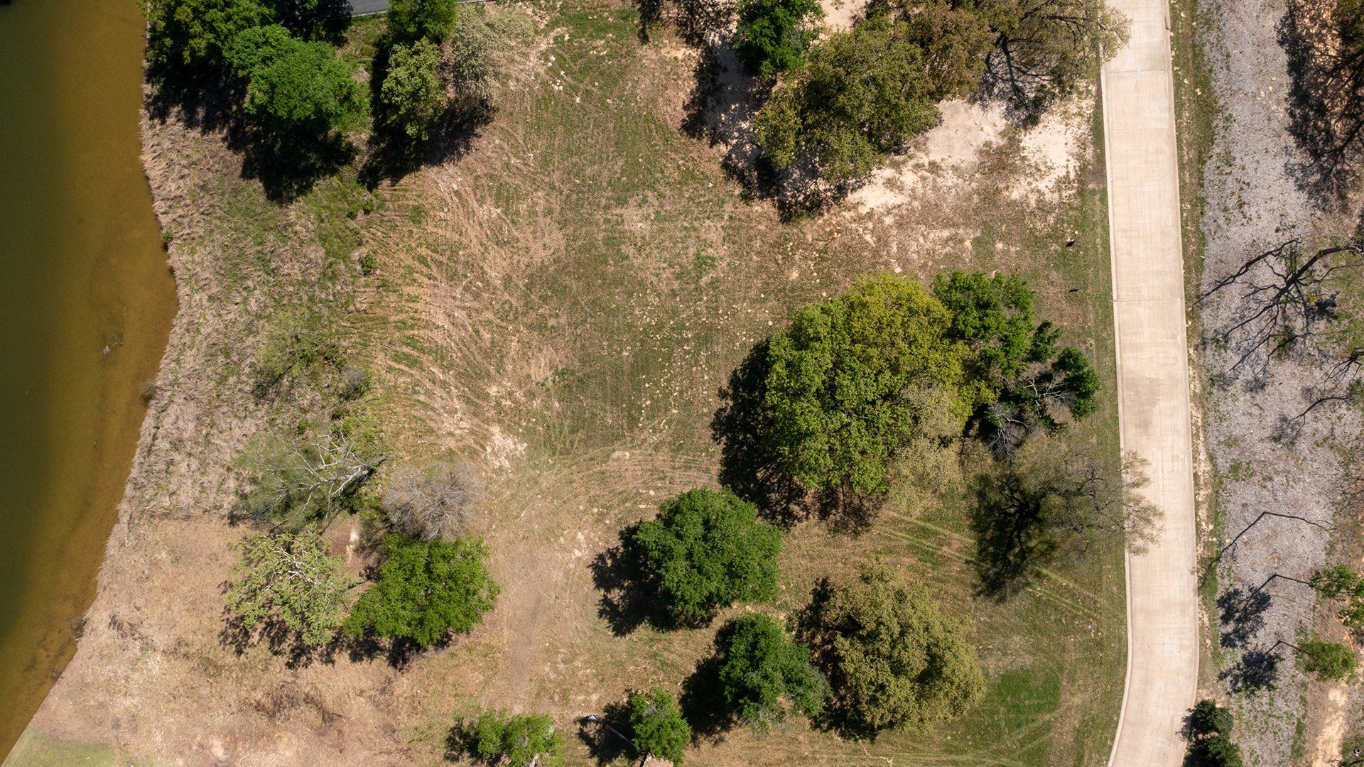 An aerial view of a dirt road leading to a lake surrounded by trees and grass.