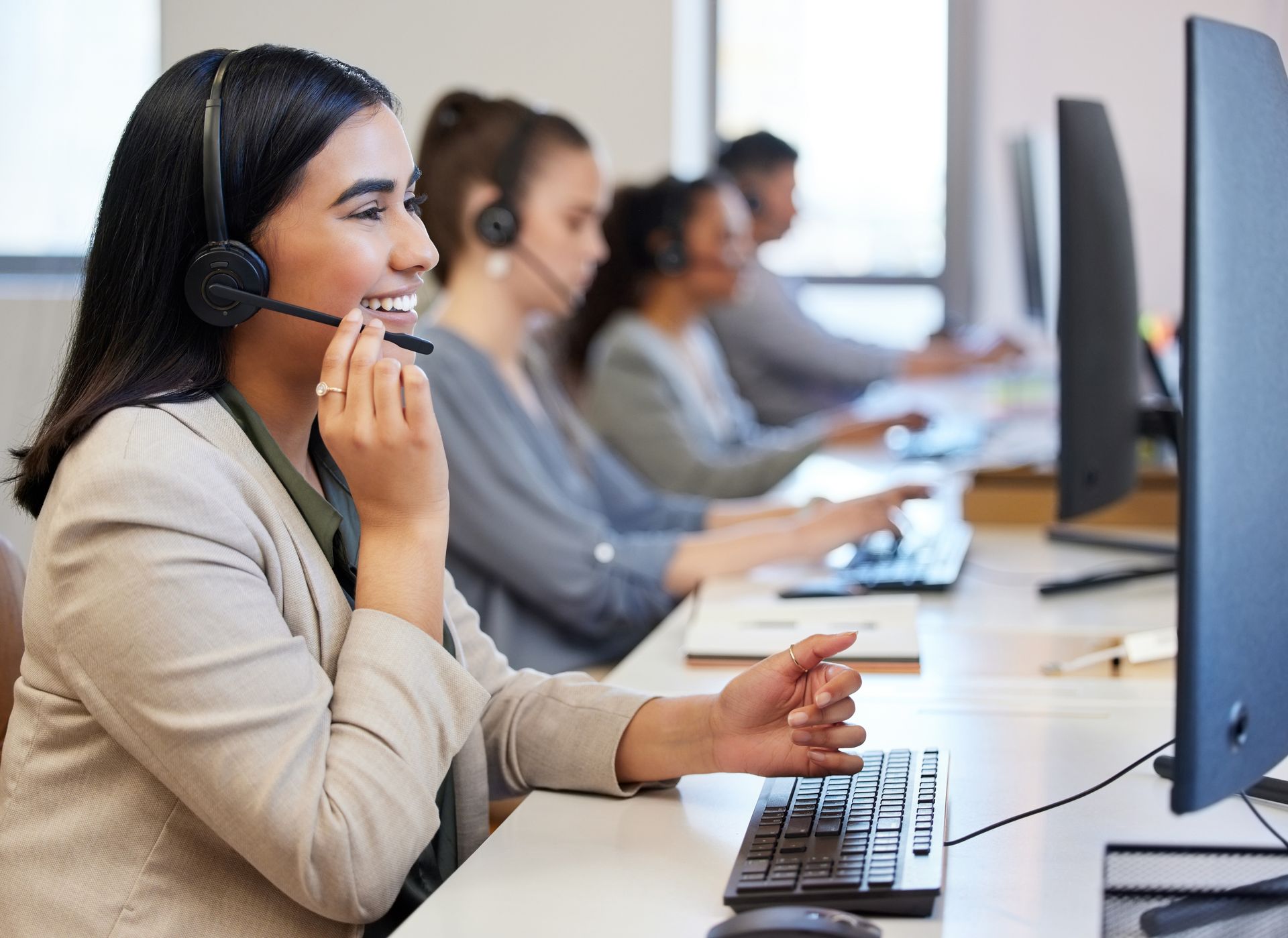 Customer support representatives wearing headsets and working on computers in an office setting.