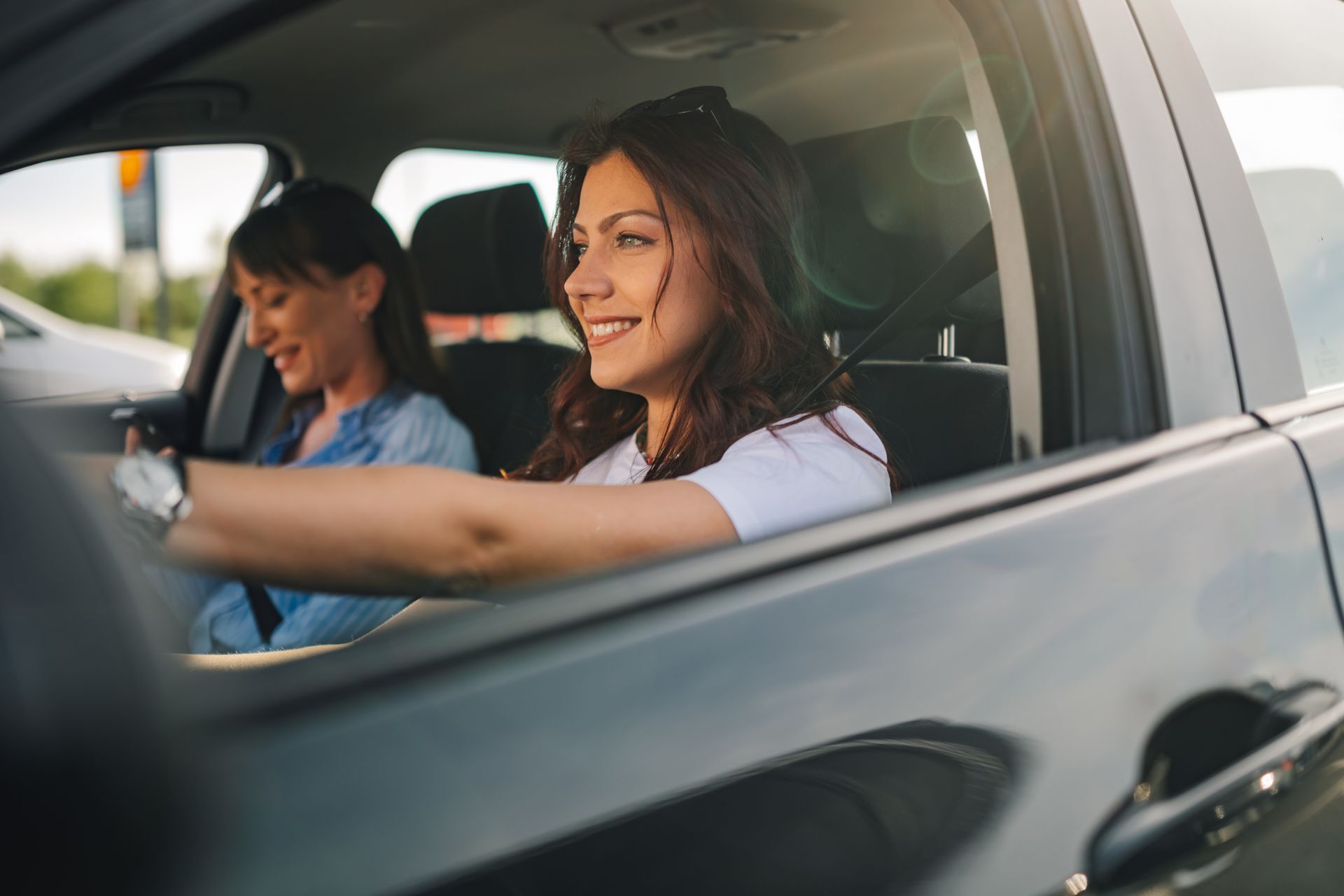 Two people smiling inside a car; the driver is holding the steering wheel and the passenger sits beside them.