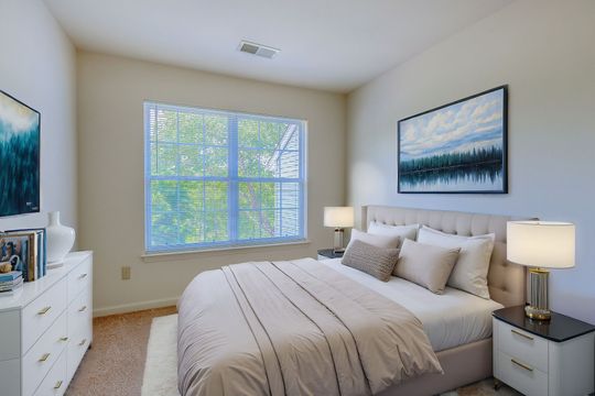 A bedroom with a bed , dresser , nightstand and two windows.