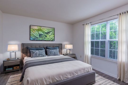 A bedroom with a large bed , two nightstands , two lamps and a large window.