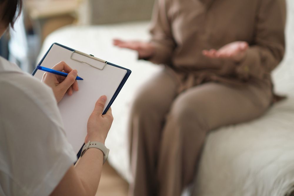A Woman is Sitting on a Couch Talking to a Doctor While Holding a Clipboard — Mount Archer Medical Centre in Berserker, QLD