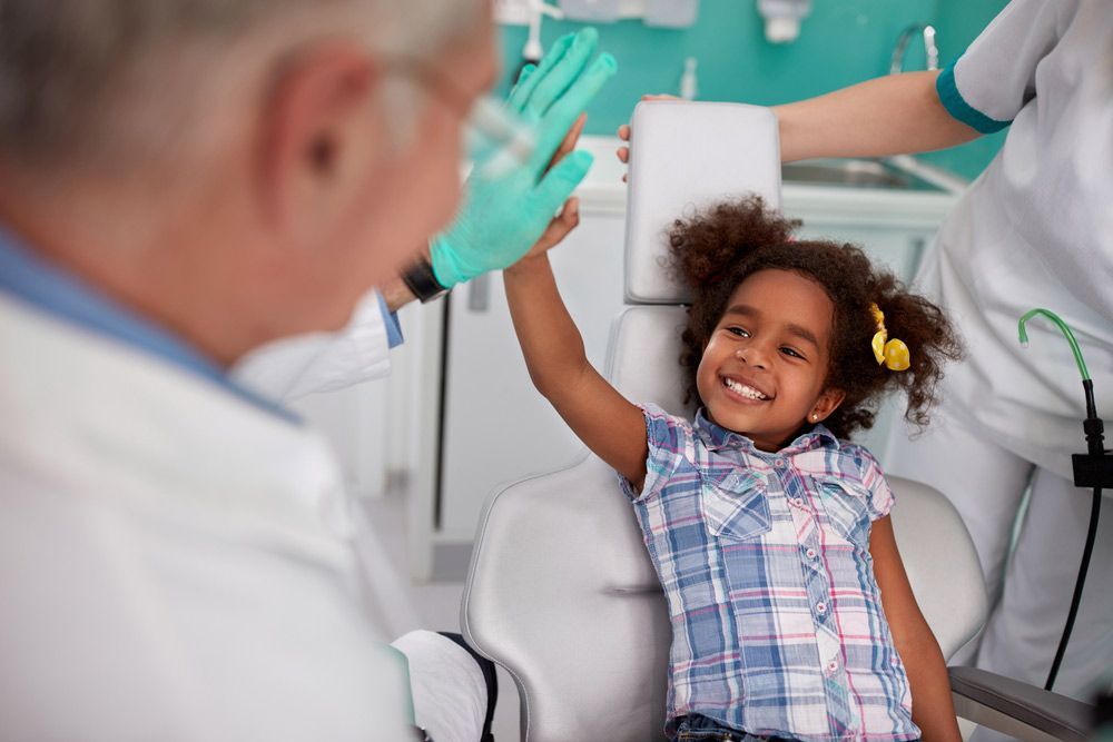 A Little Girl is Giving a High Five to a Doctor While Sitting in a Chair — Mount Archer Medical Centre in Berserker, QLD