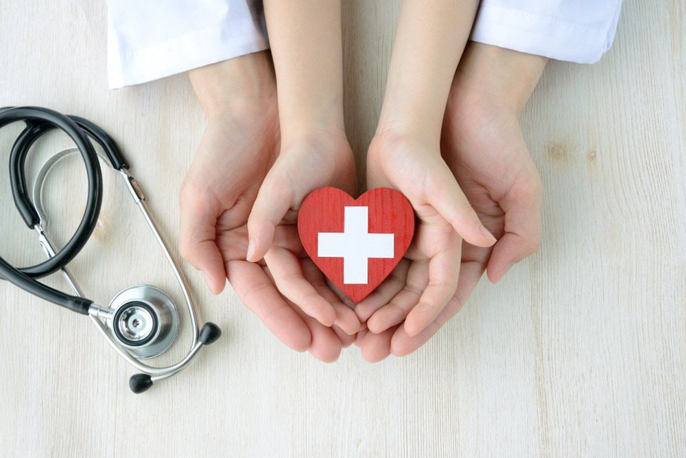 A Doctor and a Child Are Holding a Red Heart With a White Cross in Their Hand — Mount Archer Medical Centre in Berserker, QLD