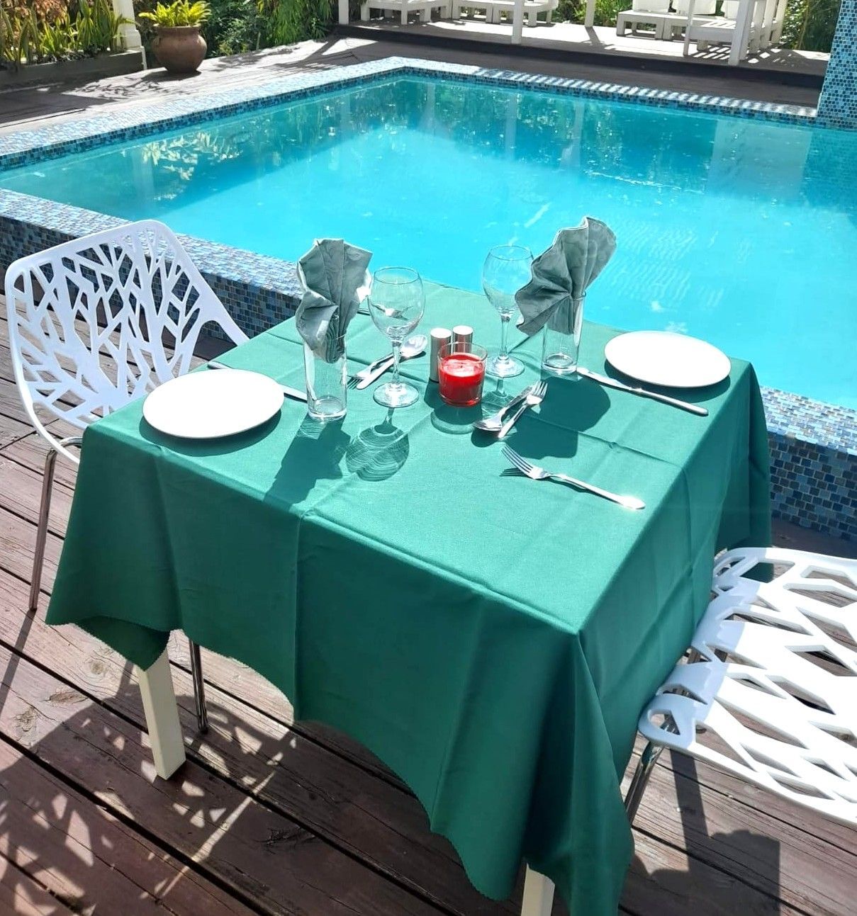 A table with plates and glasses on it in front of a swimming pool