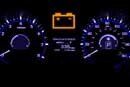 A close up of a car dashboard with a battery warning light on.