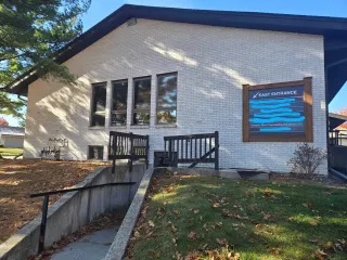 White brick building with a fenced basement entrance and a blue sign on a sunny day.