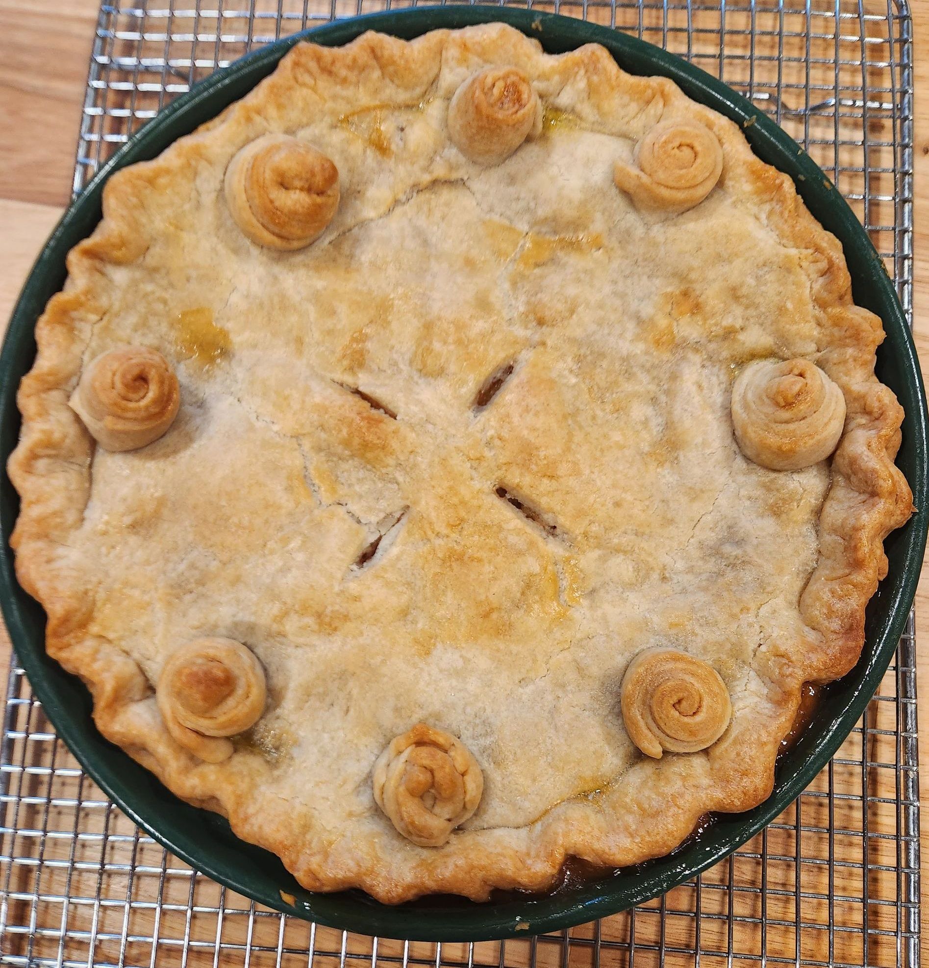 A pie with swirls on the crust is sitting on a cooling rack