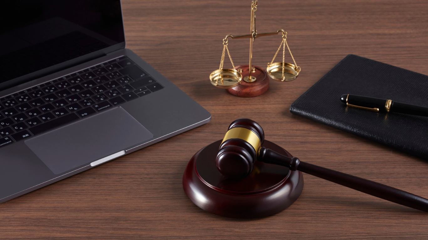 Two lawyers, one pointing at a law book, next to a balance scale, on a desk.