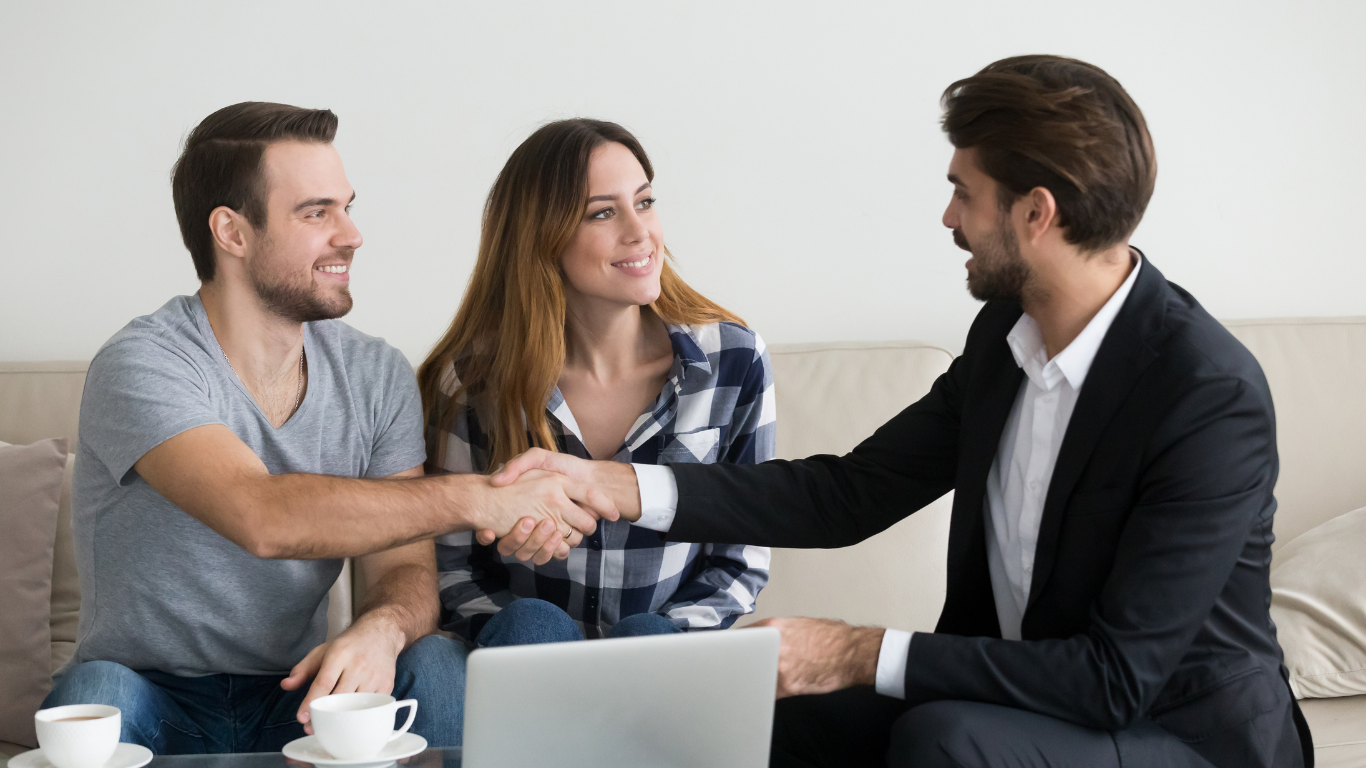 A man and woman are shaking hands with a landlord tenant lawyer in a suit while sitting on a couch.