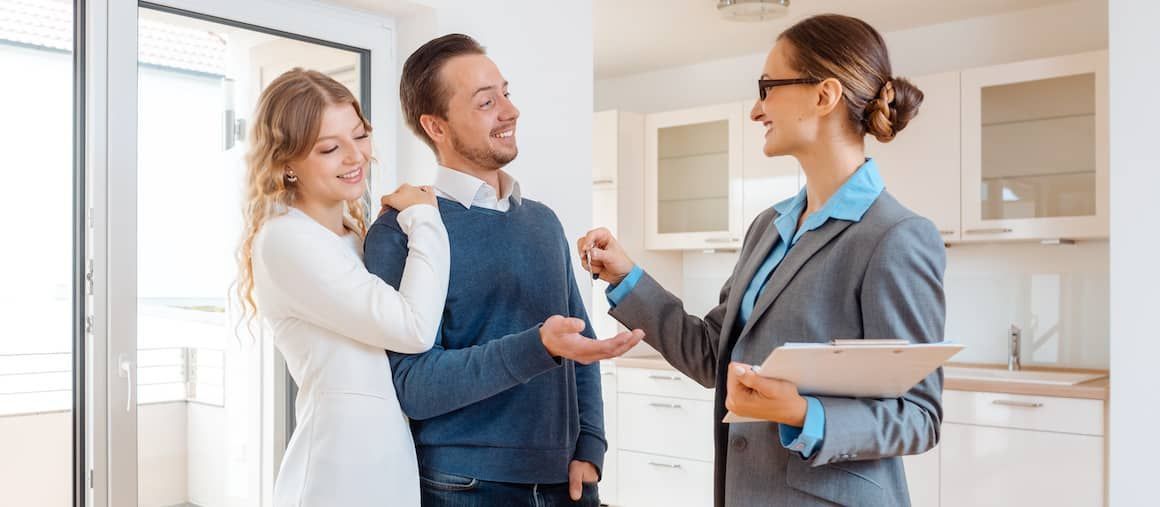 A woman is giving a man and woman keys to their new apartment.