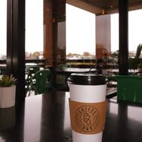 Coffee cup with a logo on a table, with outdoor view through a window.