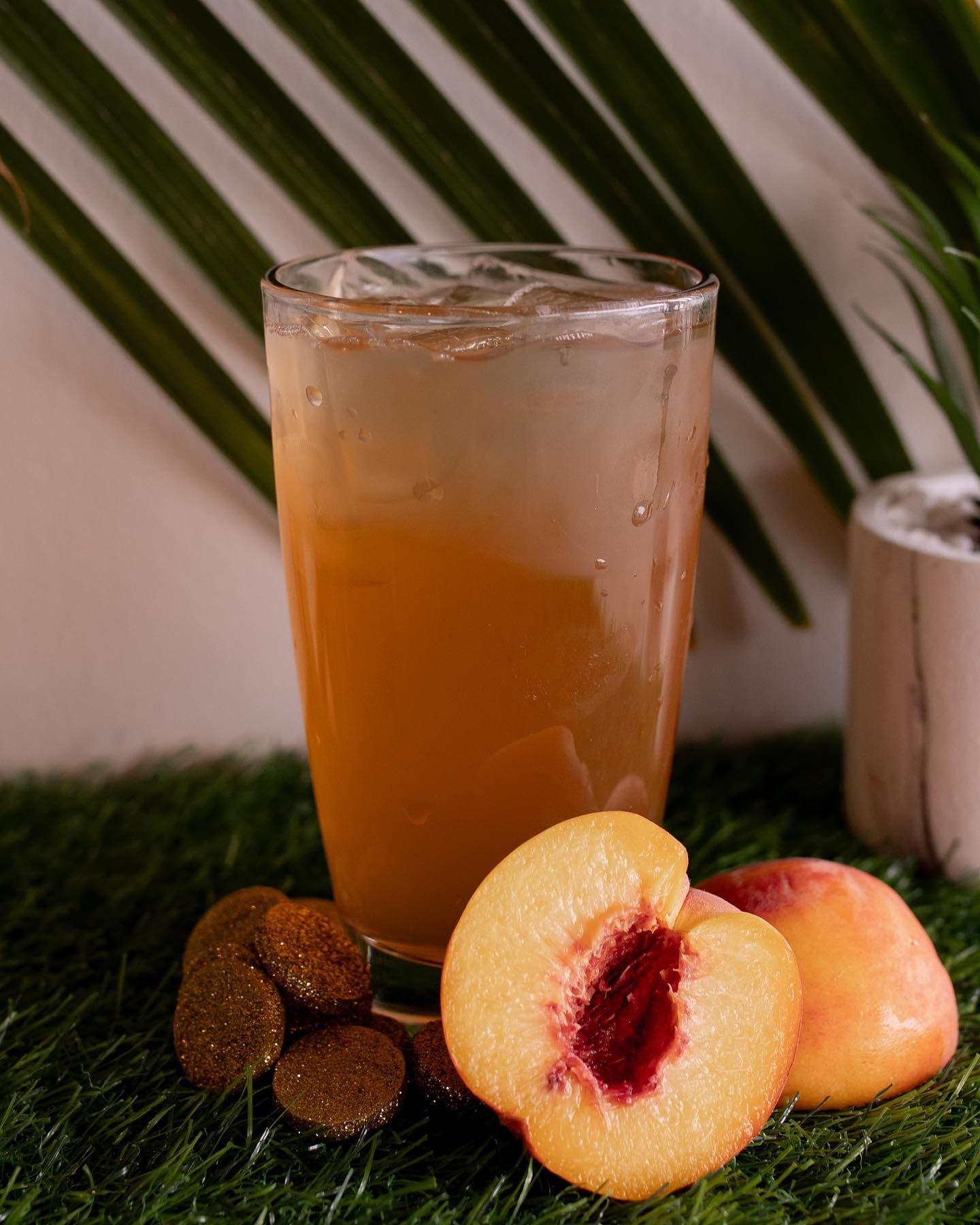 Peach drink in a glass with peach slices and green foliage, on artificial grass.