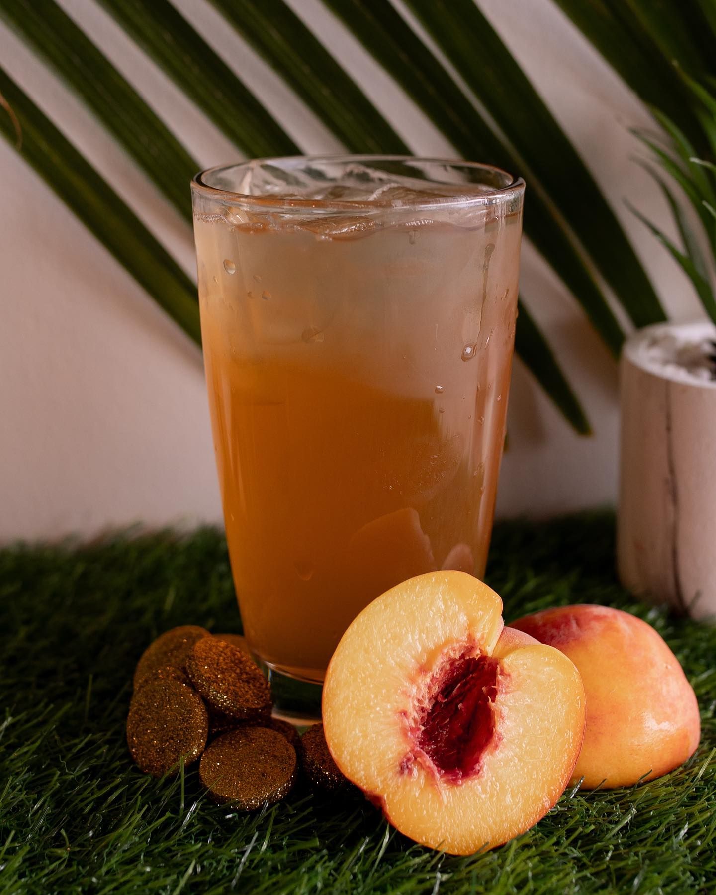 Glass of peach iced tea with peach slices on green grass.