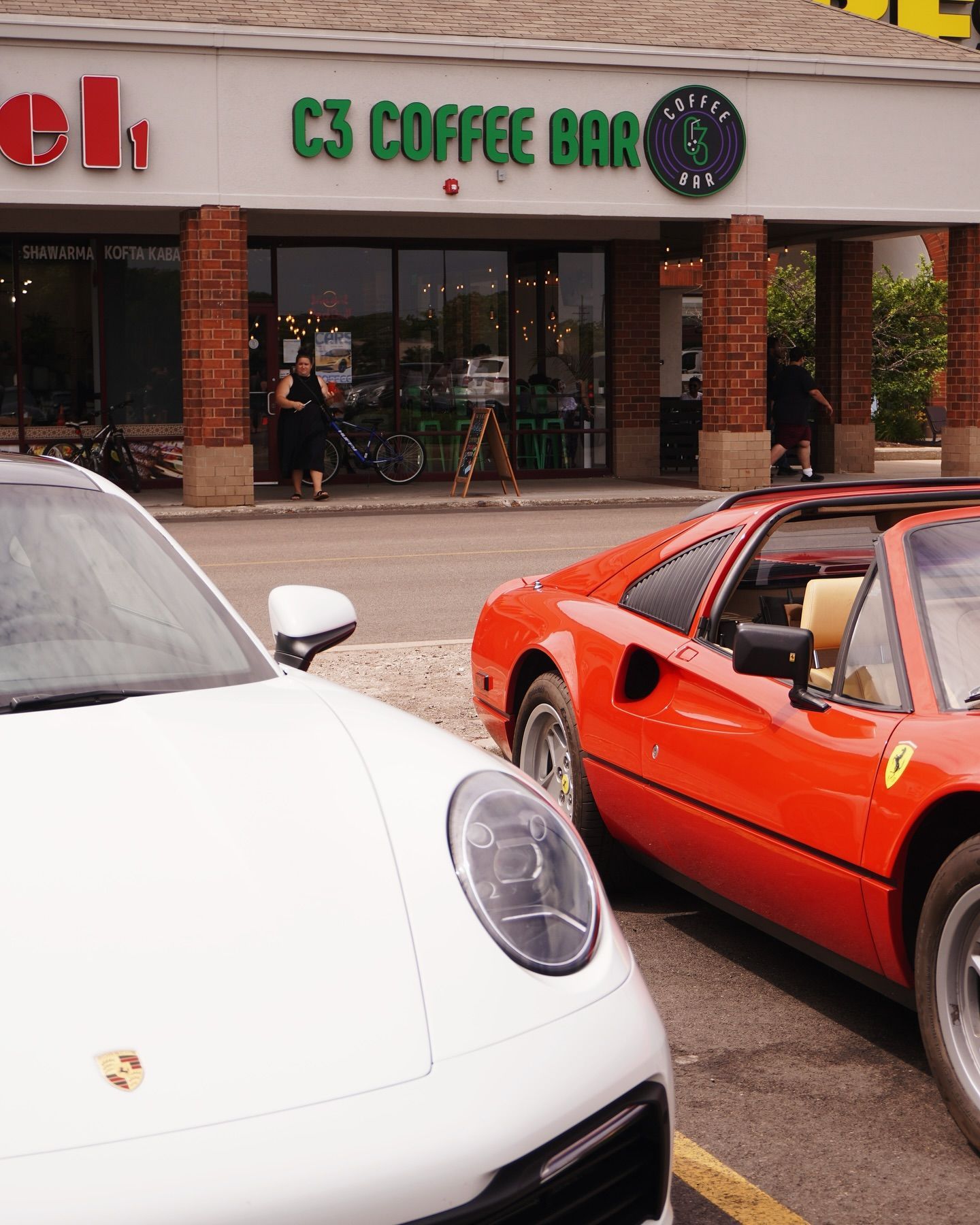 White Porsche and red Ferrari parked in front of C3 Coffee Bar.