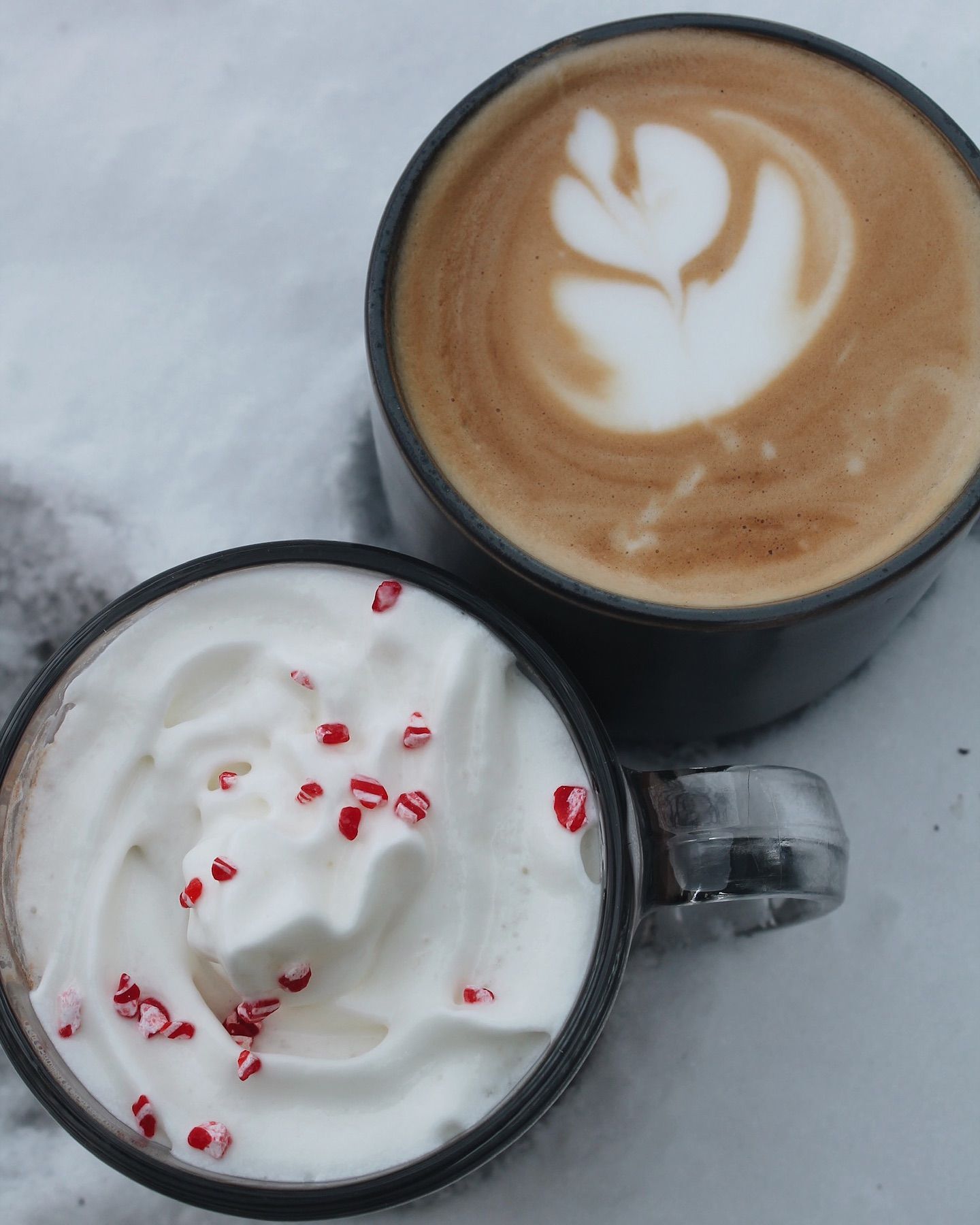 Two mugs of coffee: latte with latte art, and hot chocolate with whipped cream and crushed candy canes.