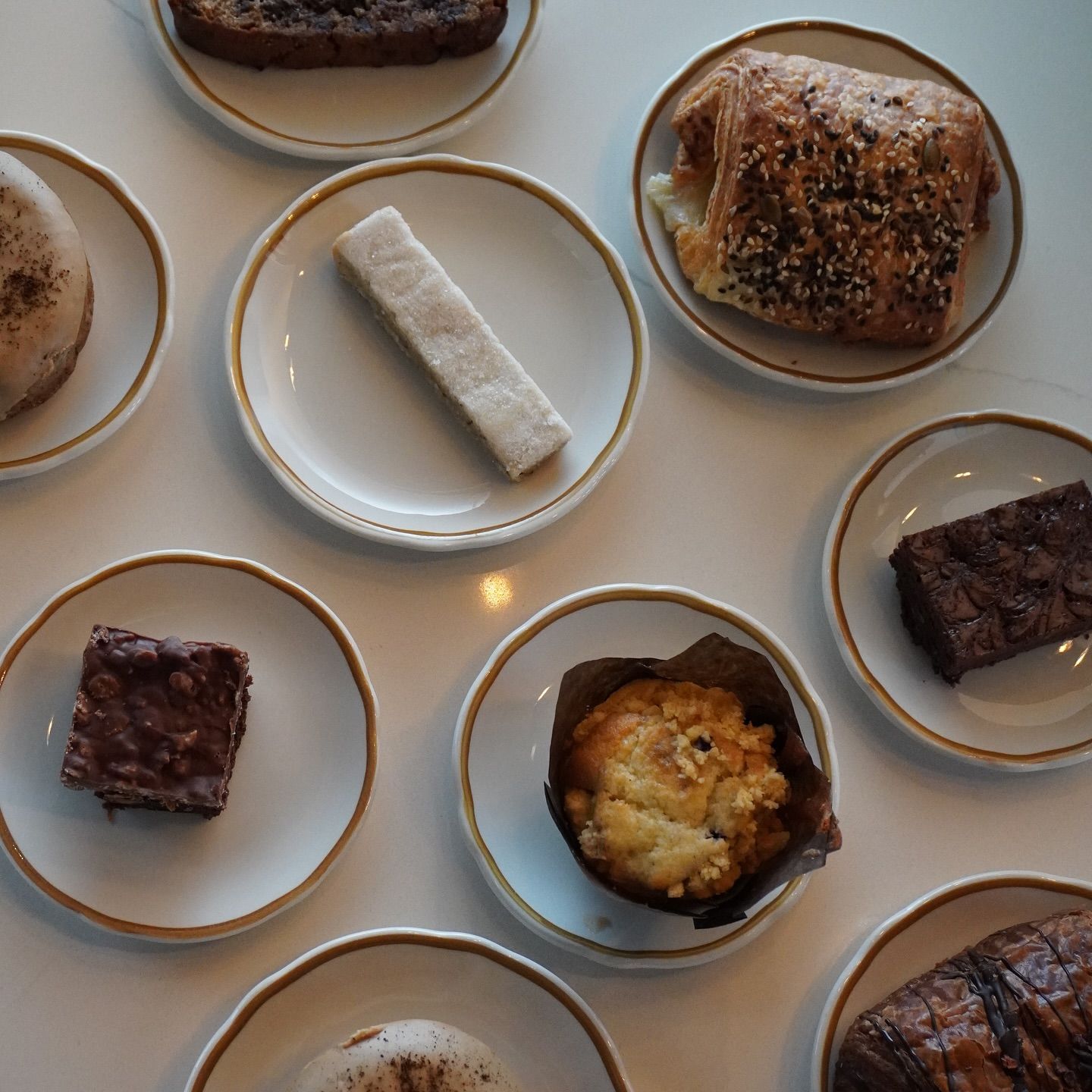 Several small plates with pastries, brownies, and muffins are arranged on a light-colored table.