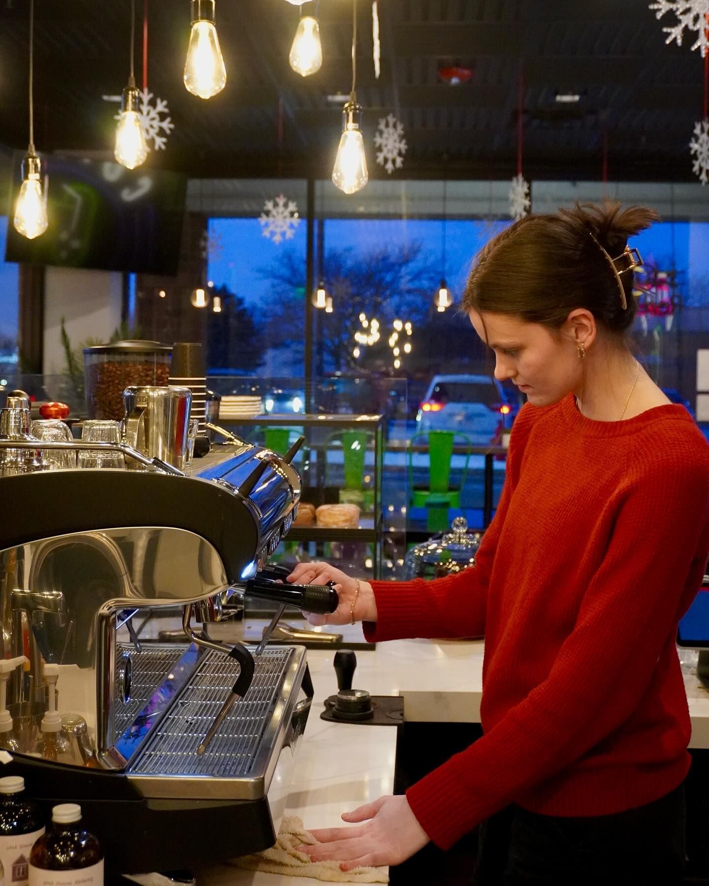 Woman in red sweater operating a coffee machine at a cafe.