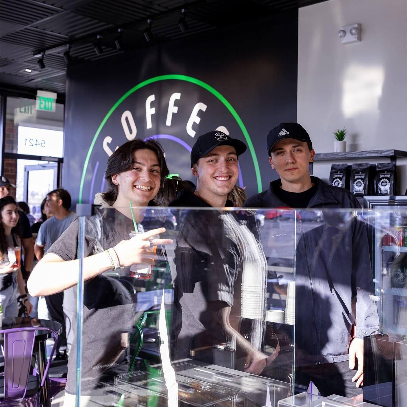 Three people behind a coffee shop counter smiling. Coffee shop logo above them.