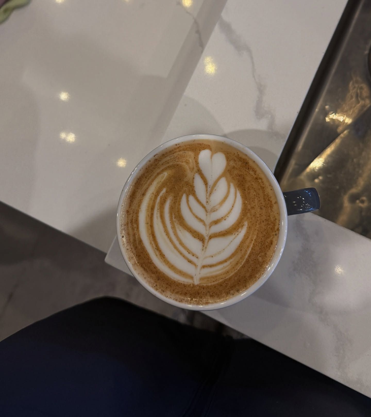 Latte with coffee art, featuring a leaf design, in a white mug on a marble table.