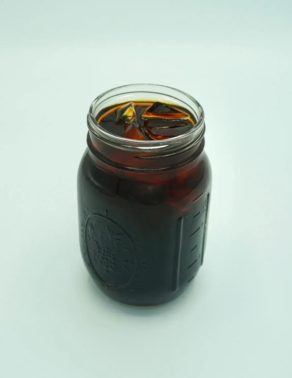 A mason jar filled with iced coffee, ice cubes visible, on a white background.