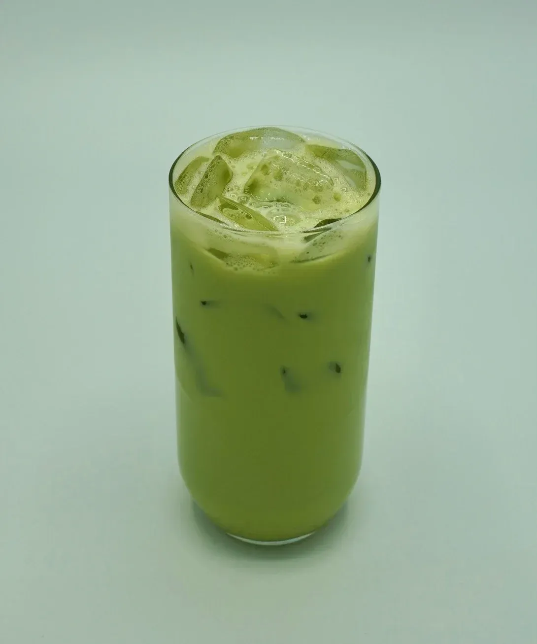 Iced matcha latte in a tall glass, pale green with ice cubes on a light blue background.