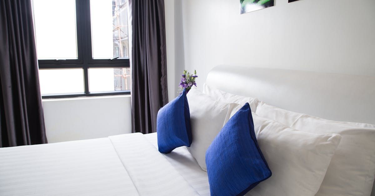 A bed with white sheets and blue pillows in a hotel room.