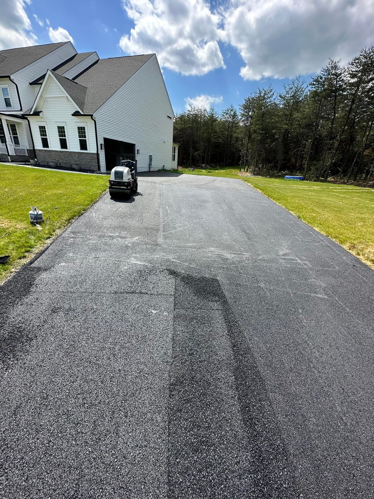 A man is driving a lawn mower down a driveway in front of a house.