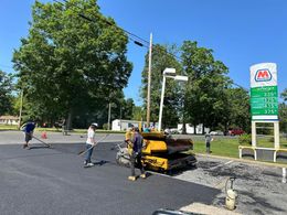 A group of people are working on a road in front of a gas station.